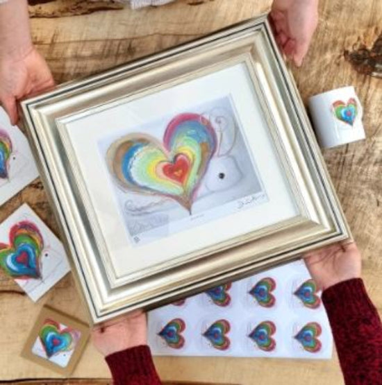 Framed artwork of a heart with a rainbow design on a wooden surface.
